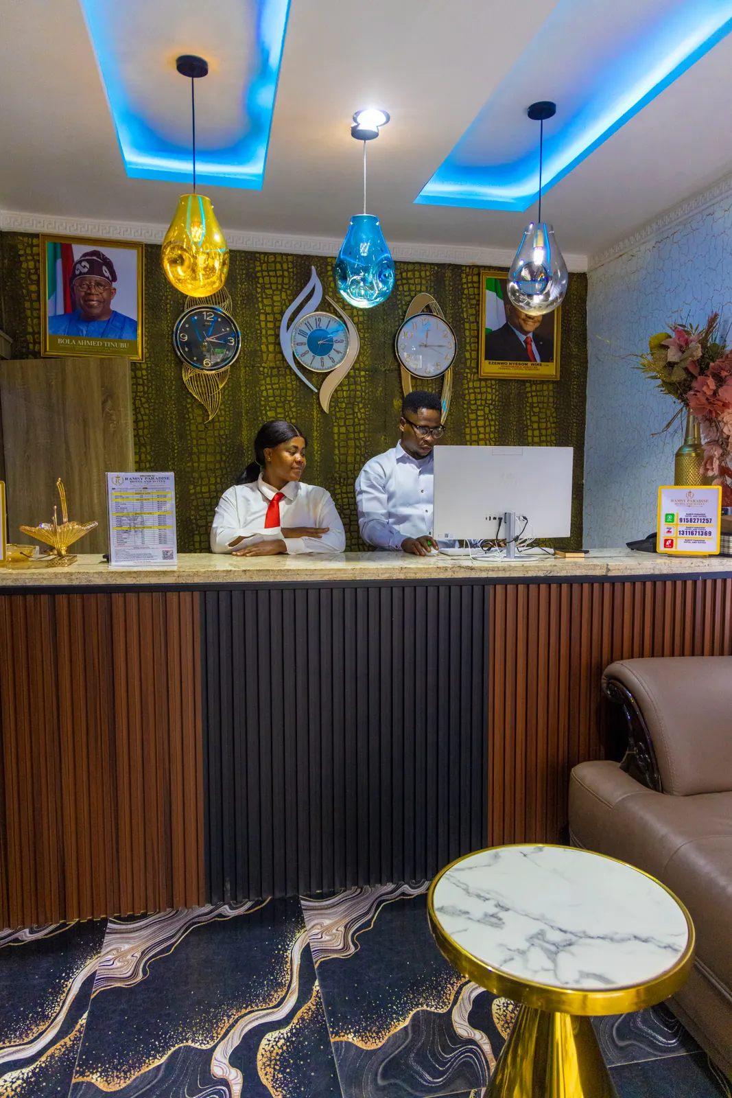 Two receptionists at the front desk, beneath blue cove lighting